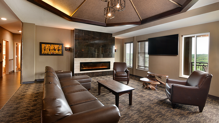 an overview of inside the Penthouse Suite's living room with tv, couch, chair, and large fireplace.