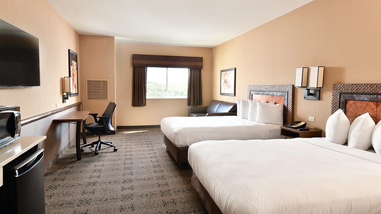 an overview of inside the Desert Room. Consists of beds, tv, windows, desk, and mini fridge.
