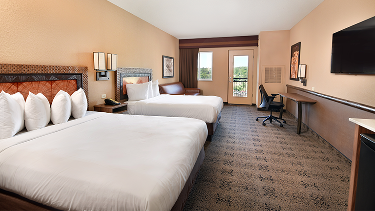 an overview of inside the Two Bedroom Suite. Consists of beds, desk, microwave, and tv.