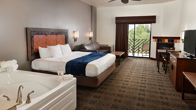 An interior of a Kalahari Resorts hotel room named the King Whirlpool featuring a king bed and balcony, and hot tub.