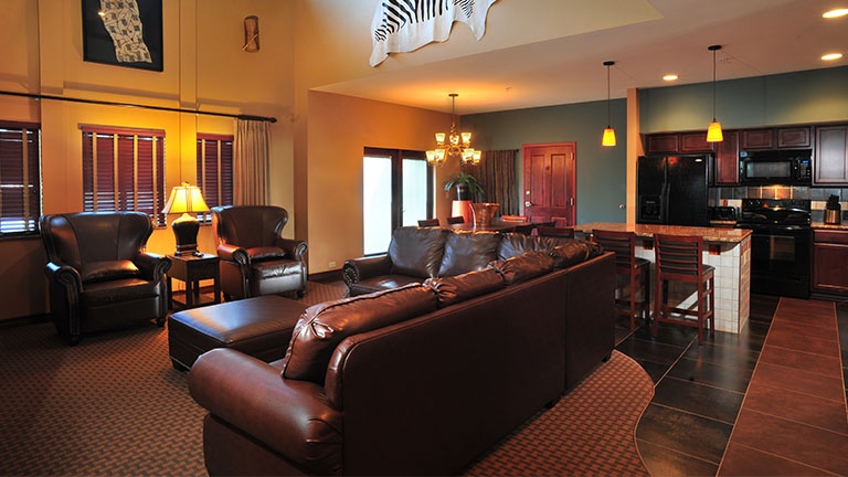 Nyumba Villa living room with a large leather couch and two chairs with a large kitchen in the background