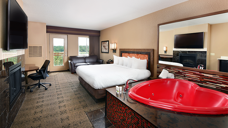 an overview of inside the Honeymoon Suite. Consists of bed, desk, tv, mirror, and heart-shaped tub.